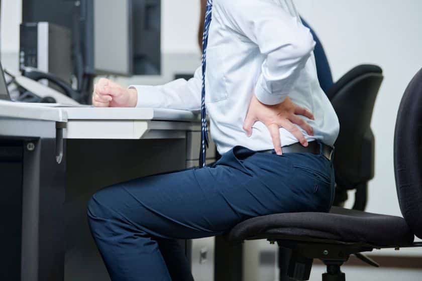 A man in a suit experiences back pain at his desk